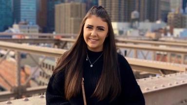 young person leaning against railing of a bridge, city landscape behind them